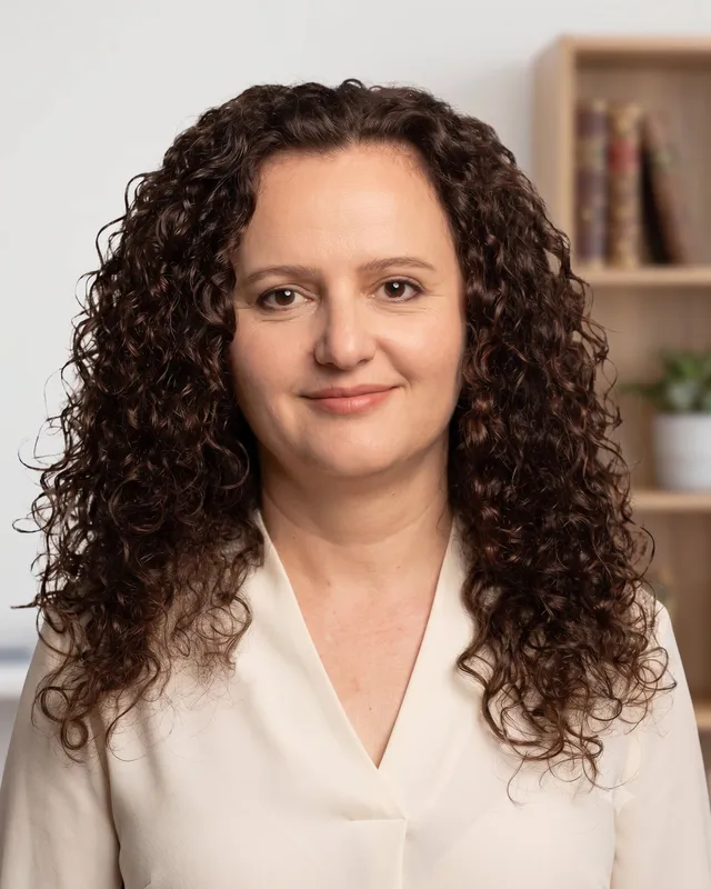 A professional studio portrait of a female trainer specialized in financial management, with curly dark hair, wearing a cream blouse.